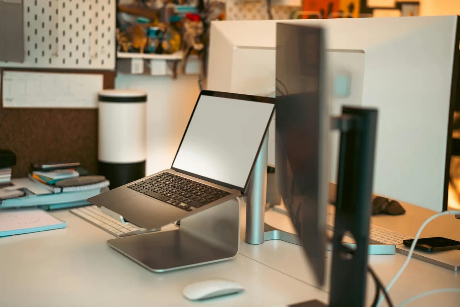 A compact coworking desk setup with a laptop on a stand, external keyboard, mouse, and headphones