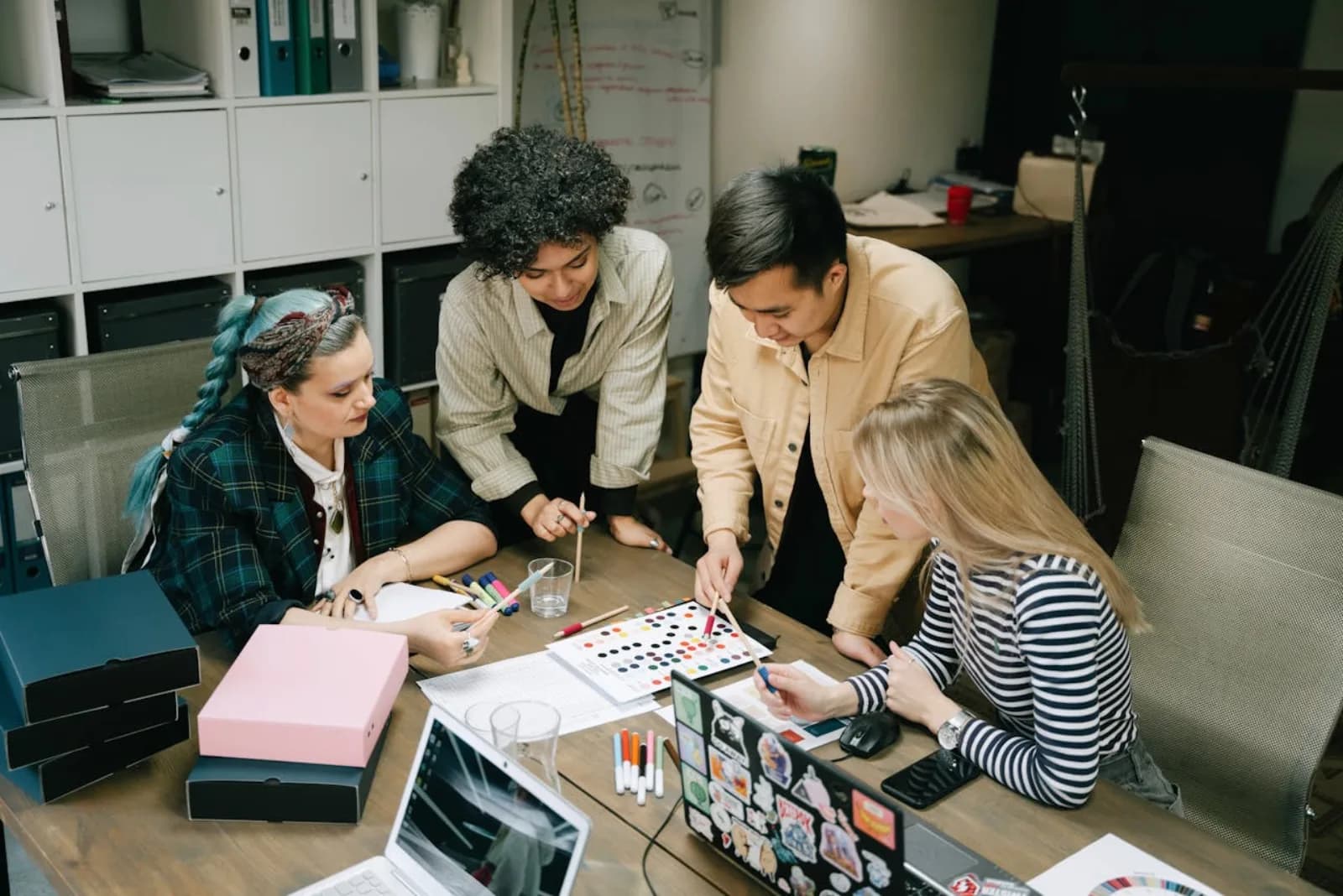 A small mixed group of remote workers collaborating around a laptop at a casual co-working space, one person pointing at the screen