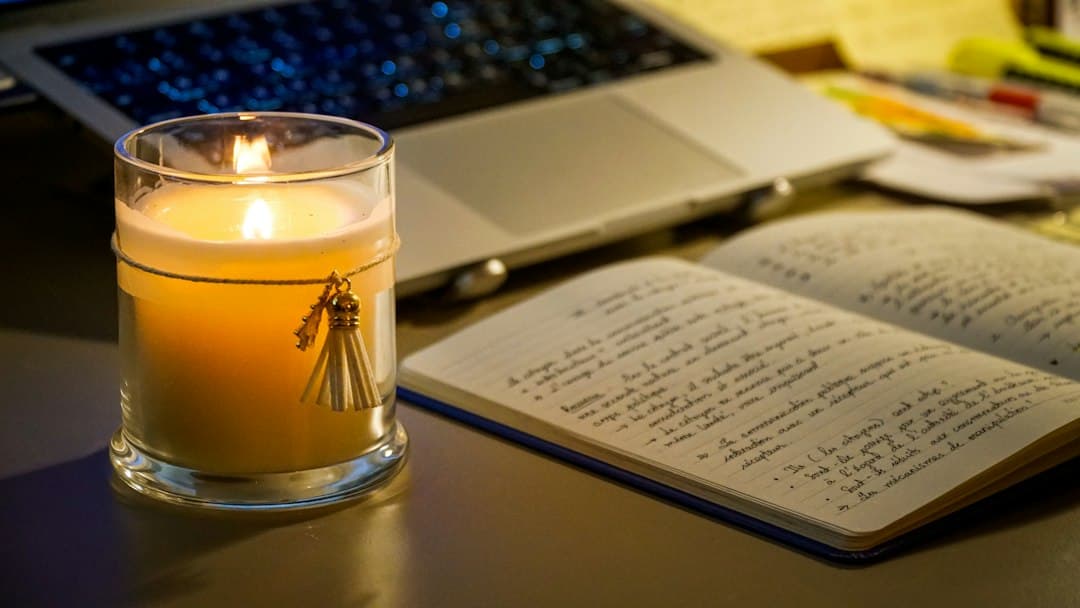 Laptop and notebook lit by a candle on a desk during a power outage.