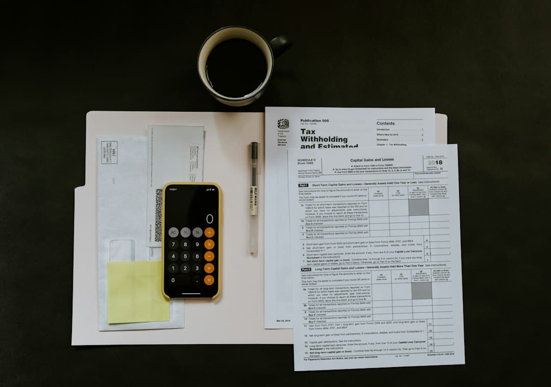 Tax forms and a calculator on a desk with a coffee cup and sticky notes.