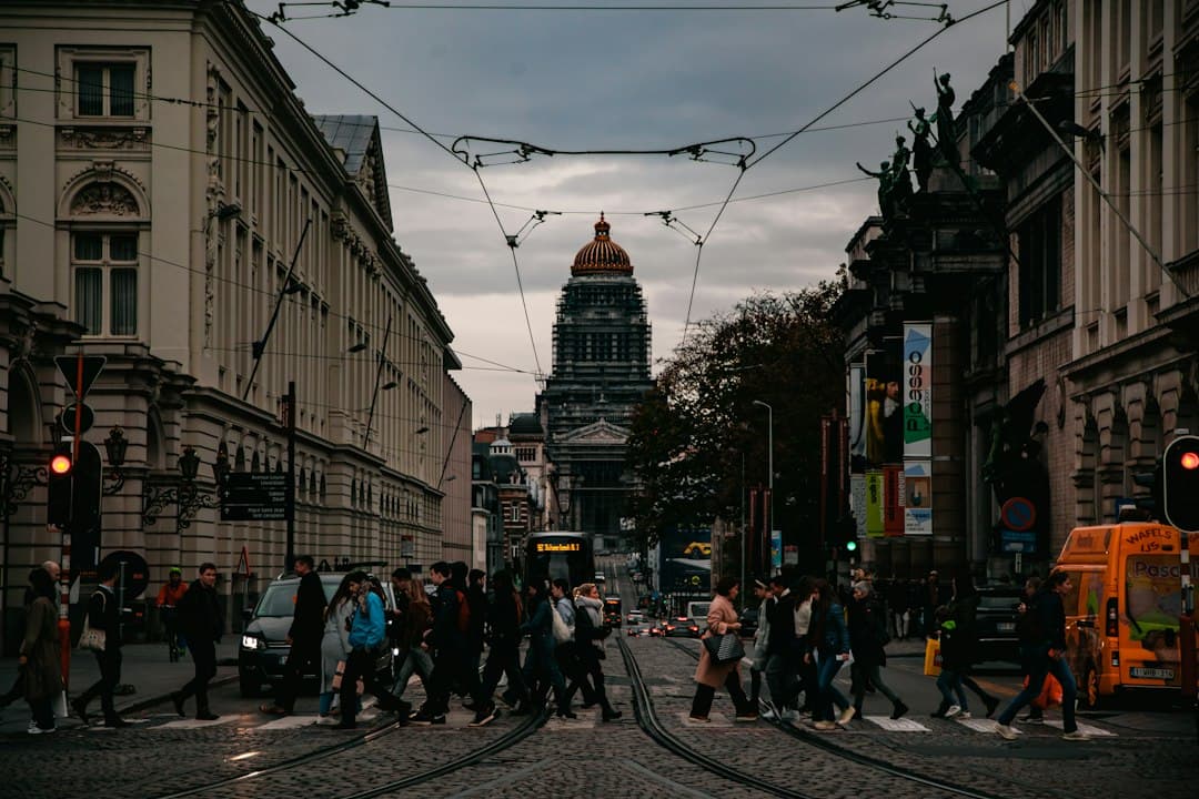 Busy street in a European city with pedestrians, historic facades, and a domed cathedral in daylight.