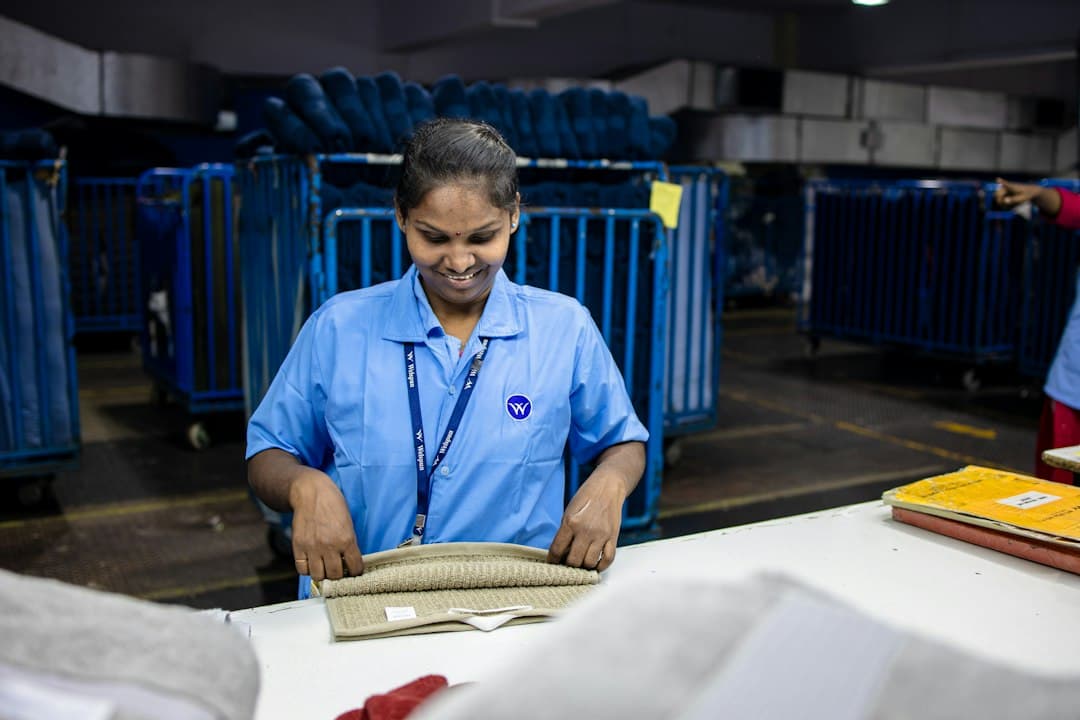 Agent postal inspectant un textile sur une table dans un centre de tri avec chariots bleus en arrière-plan.