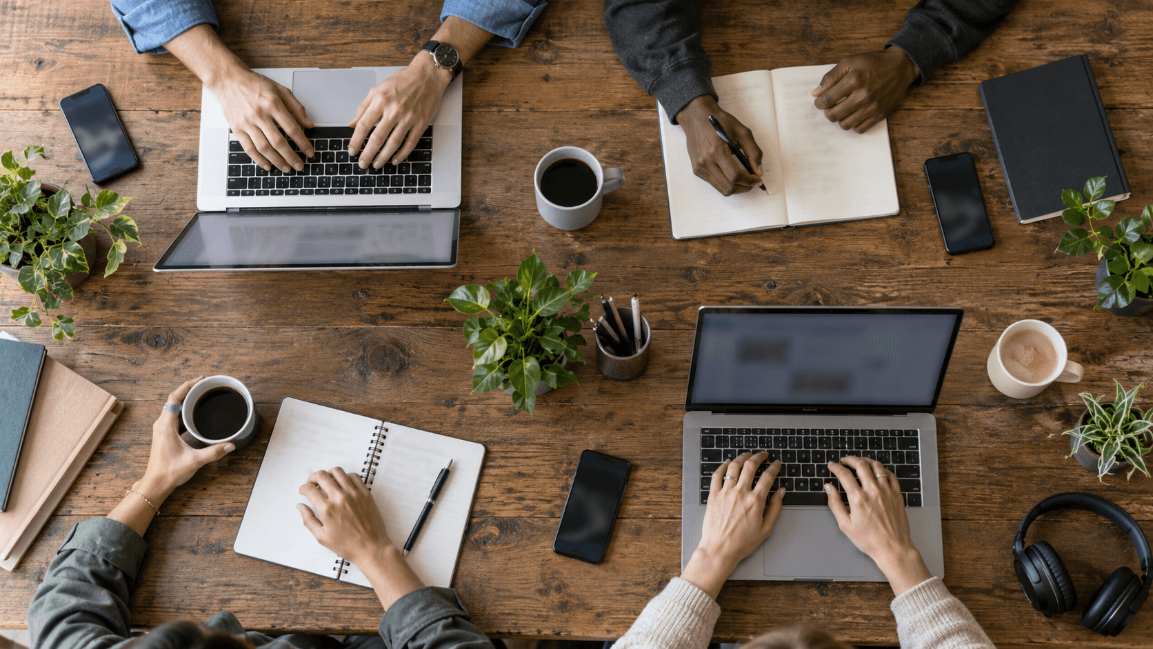 Nómadas digitales trabajando juntos en una mesa de madera con portátiles, café y cuadernos en un espacio de coworking.
