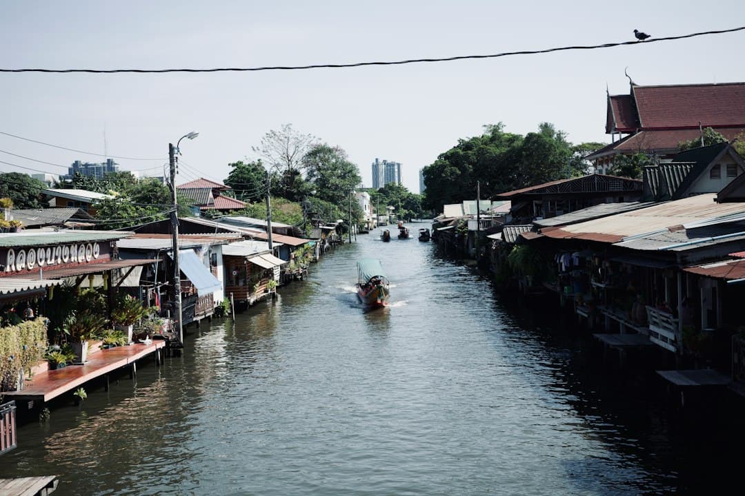 Maisons traditionnelles construites le long d'un canal en Thaïlande avec un bateau qui passe.