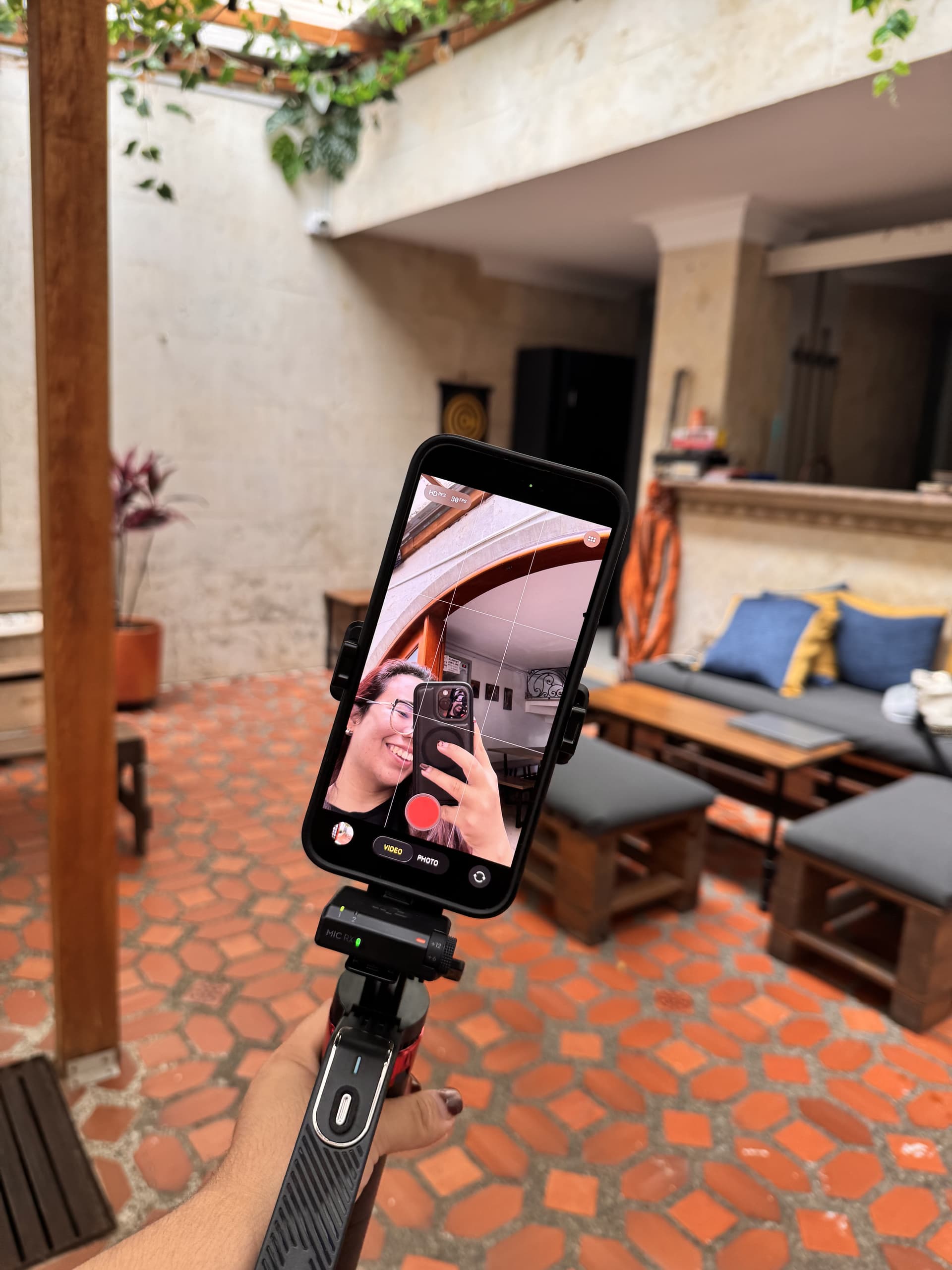 Daniela Morán filming herself with her smartphone mounted on a stabilizer, in a patio with terra cotta flooring.