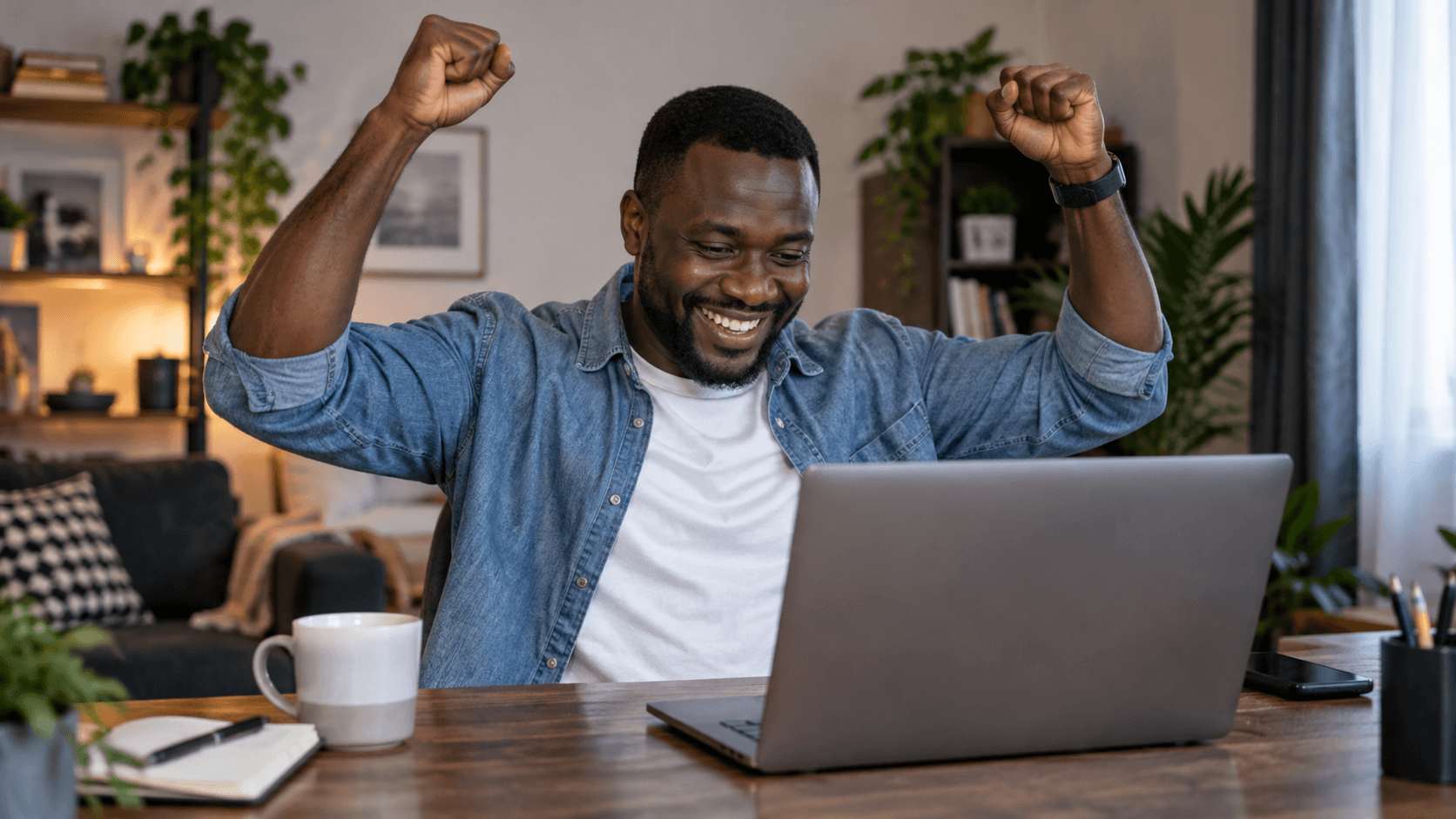Télétravailleur célébrant son succès à son bureau à domicile avec ordinateur portable et tasse de café.