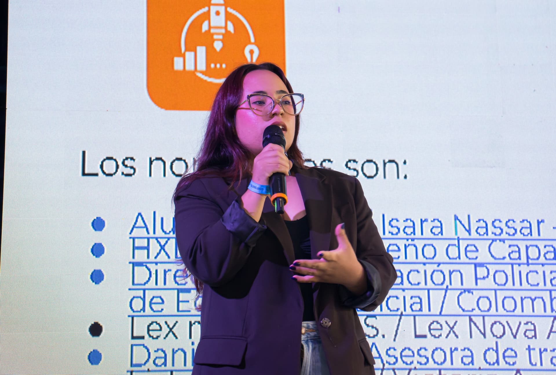 Daniela Morán speaks into a microphone in front of a presentation screen.