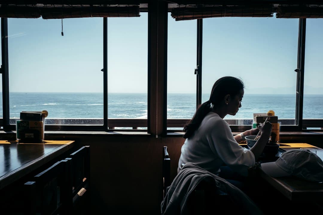 Digitale nomade die op een laptop werkt naast een raam met uitzicht op de zee op een Grieks eiland.