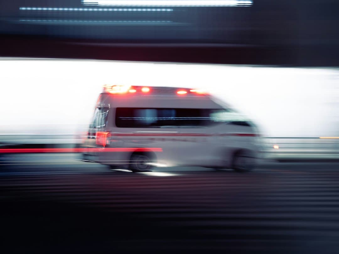 Ambulancia con luces rojas y azules encendidas circulando de noche por una calle urbana.