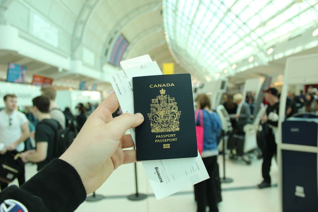 Hand holding a Canadian passport with documents in an airport terminal, symbolizing immigration and travel.