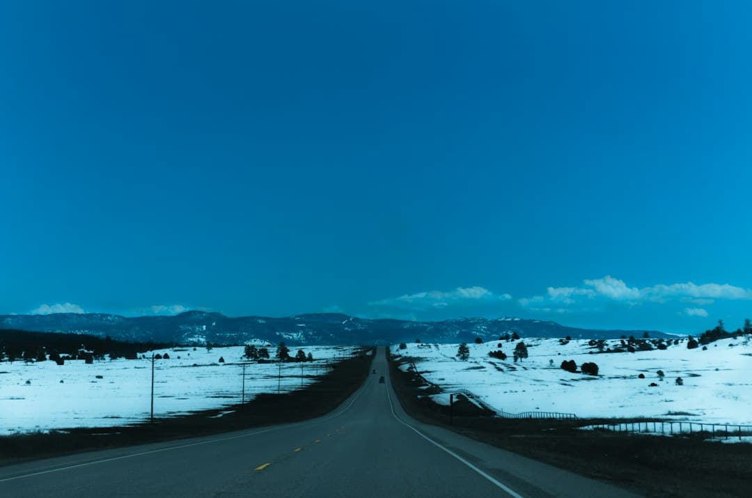 A long, straight road crossing a snowy landscape under a vast blue sky in the United States.