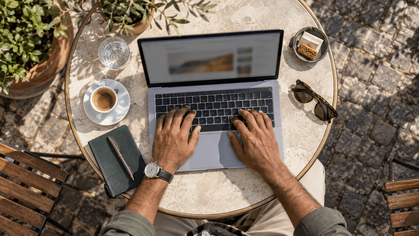 Digital nomad typing on a laptop at an outdoor café table with coffee and accessories