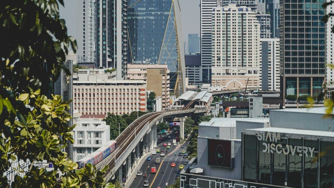 Train BTS surélevé au-dessus d'une avenue de Bangkok avec circulation et skyline urbain.