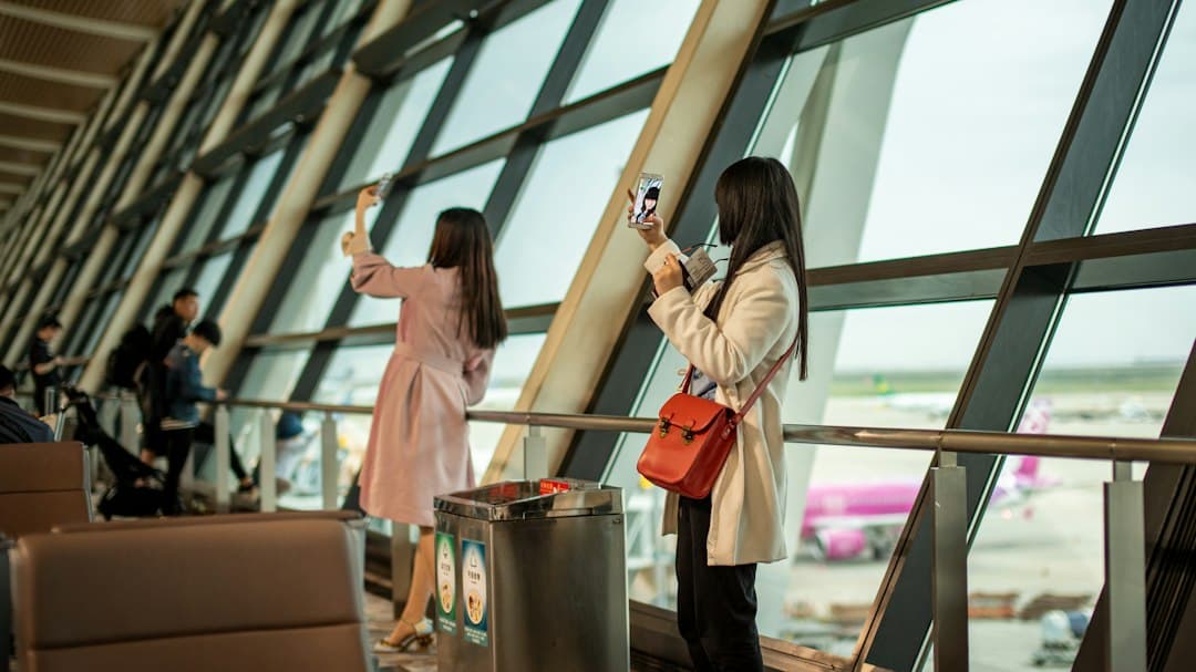 Deux femmes prenant des photos avec leur smartphone dans un terminal d'aéroport près d'une grande baie vitrée.