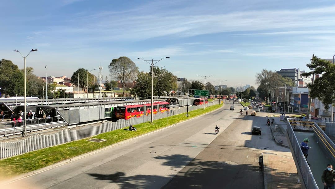 Red TransMilenio articulated bus at a Bogotá station with waiting passengers and modern infrastructure.