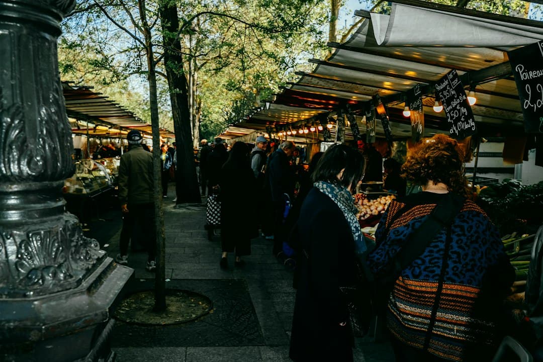 Lively outdoor French market with vendors and customers under covered stalls and trees.