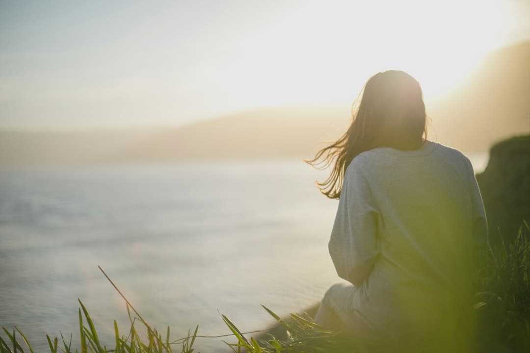 A woman sitting alone on a cliff edge overlooking the sea at sunset.