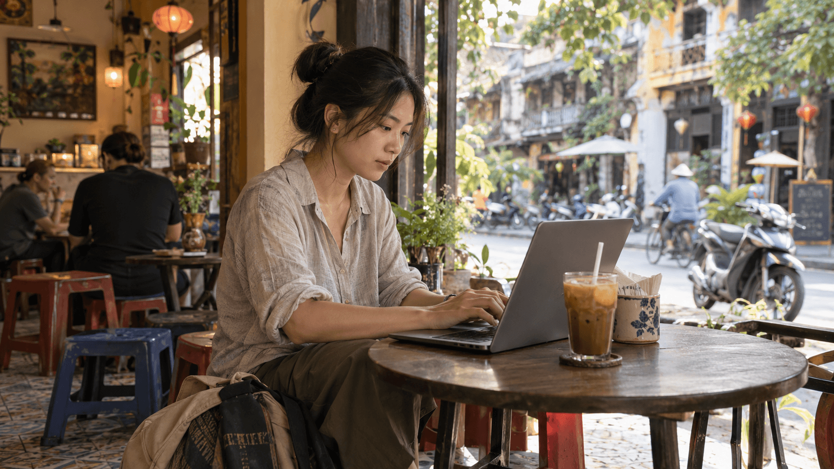 Digital nomad working on a laptop in a Vietnamese café with an iced coffee.