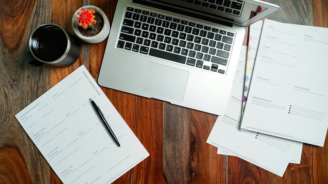 Ordinateur portable et documents fiscaux sur bureau en bois avec café et plante pour espace de travail.