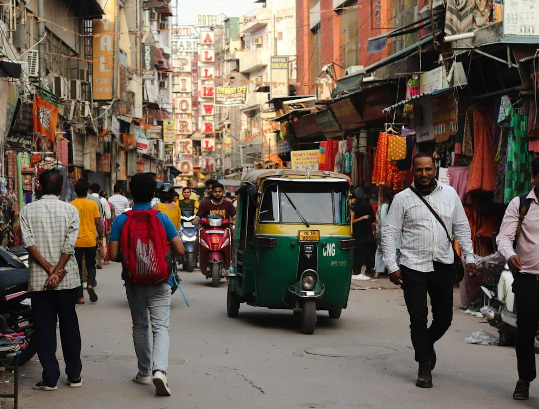 Rue animée indienne avec auto-rickshaw, piétons et enseignes colorées dans une zone de marché urbain dense.
