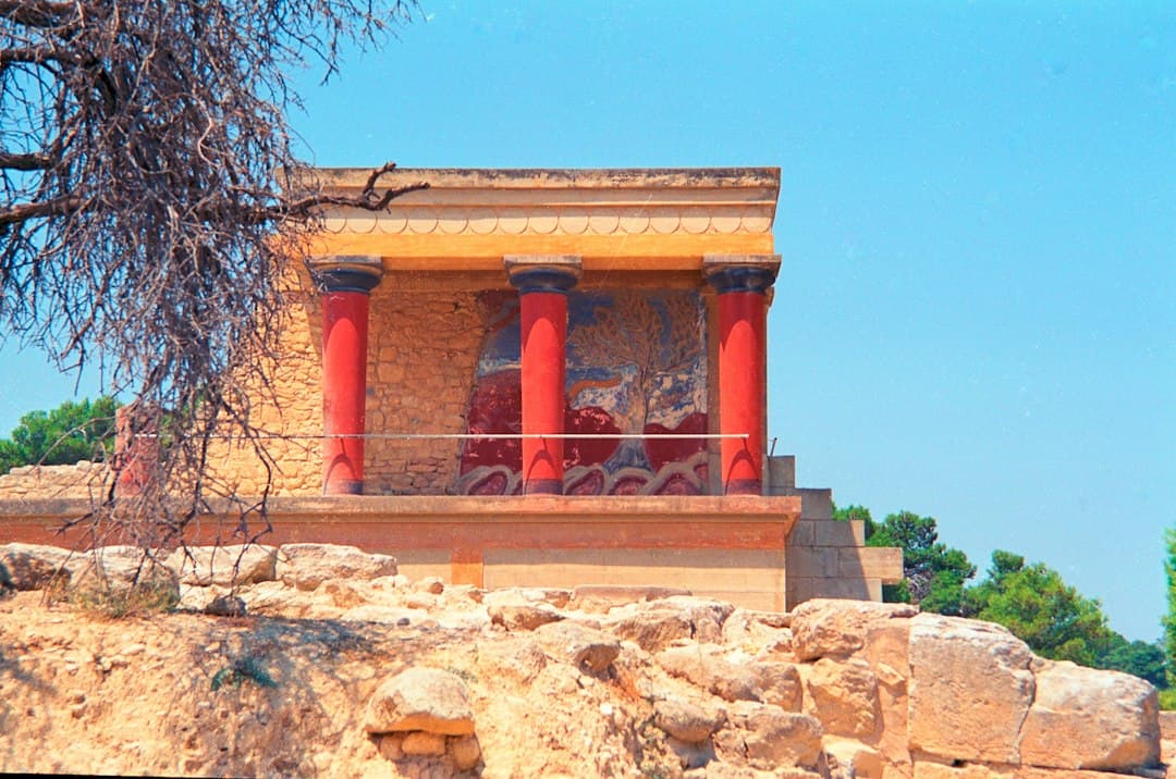 Ruïnes van het paleis van Knossos met rode zuilen onder een helderblauwe hemel, weinig bezoekers zichtbaar