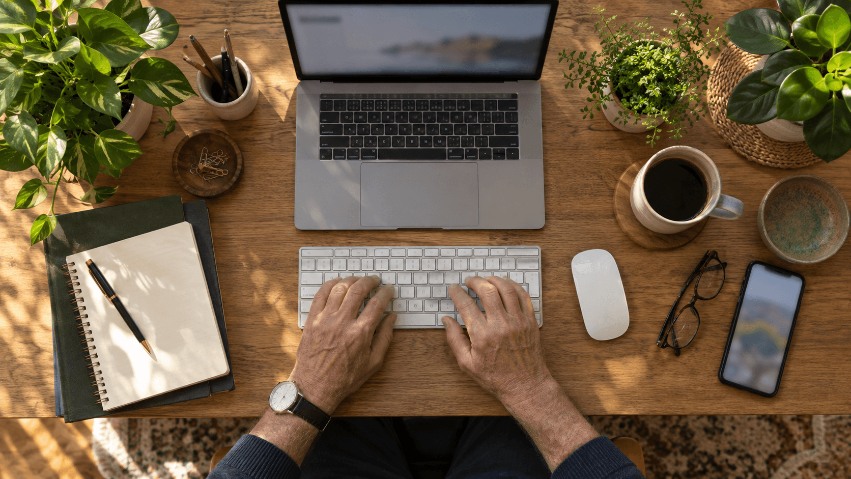 Espace de télétravail avec ordinateur portable, plantes, café et lumière naturelle à un bureau en bois.