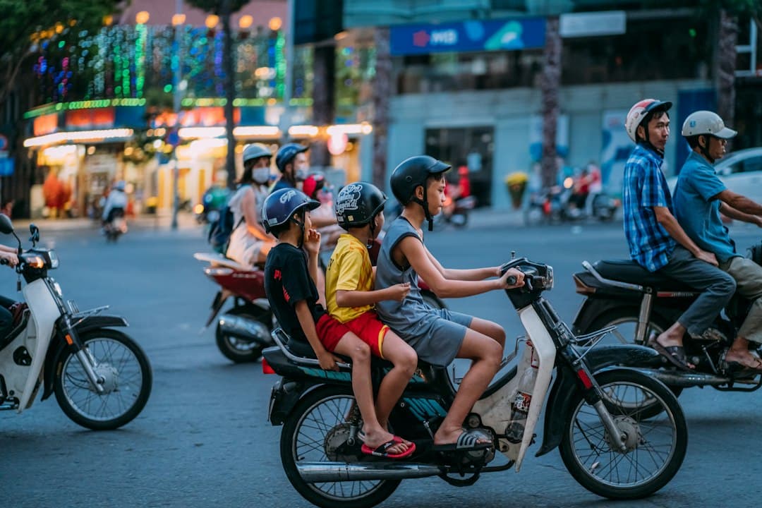 Scooter riders on a busy street in Ho Chi Minh City at dusk, with illuminated shops in the background.