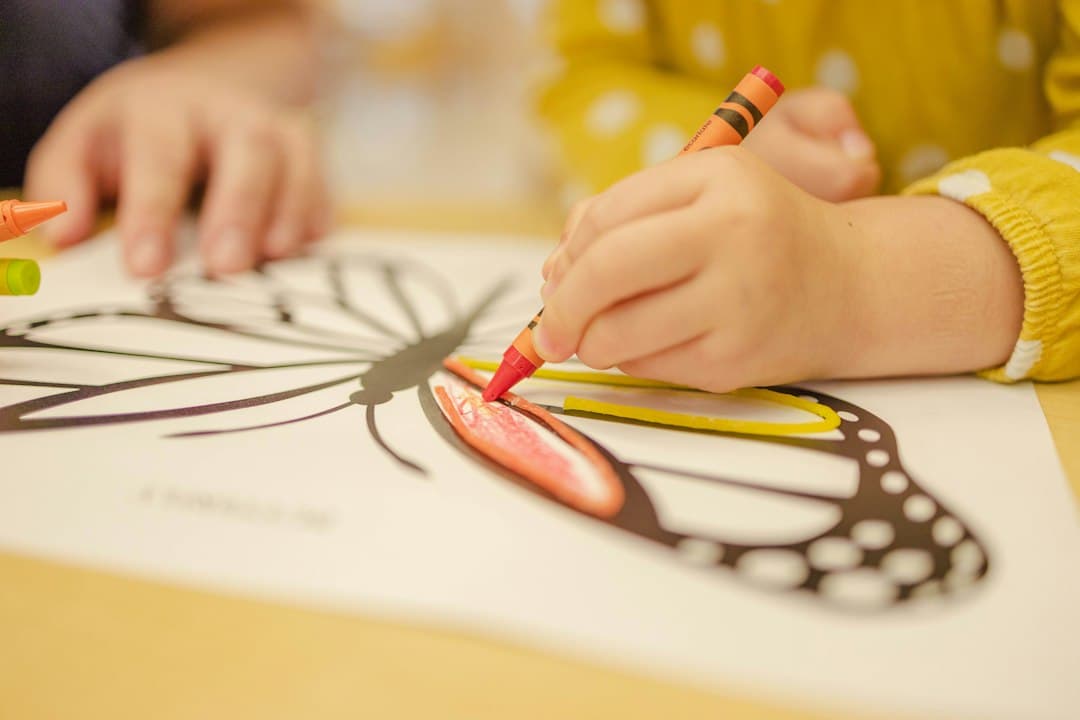 Enfant coloriant un dessin de papillon avec des marqueurs à table pendant une activité créative.