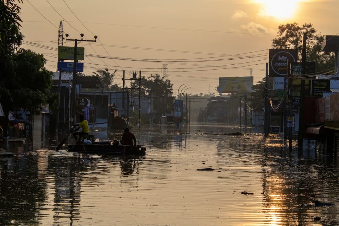 Deux personnes sur une petite barque naviguant dans une rue inondée au coucher du soleil.