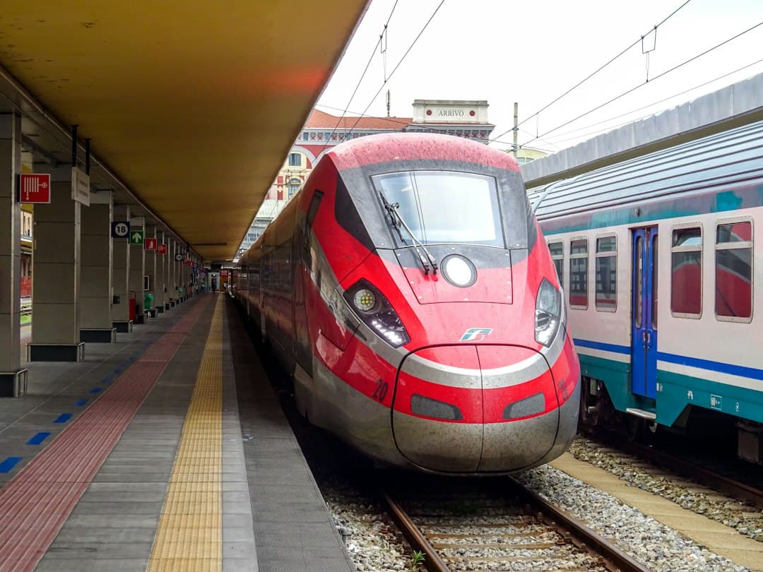 Treno Frecciarossa rosso ad alta velocità su un binario di una stazione italiana con linee elettriche aeree.