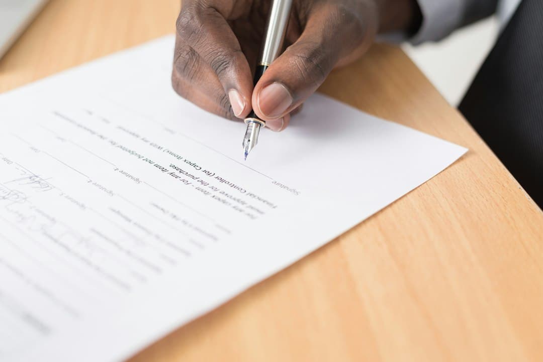 Person signing a rental contract with a pen on a wooden table.