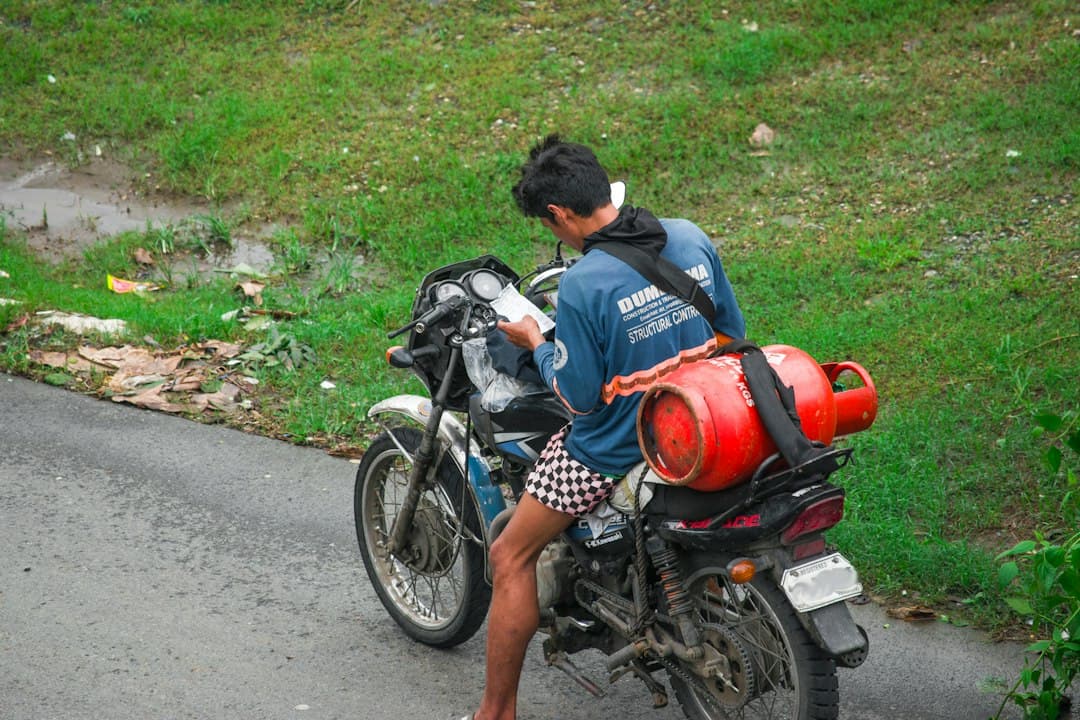 A man on a motorcycle carrying a red gas bottle on a rural road.
