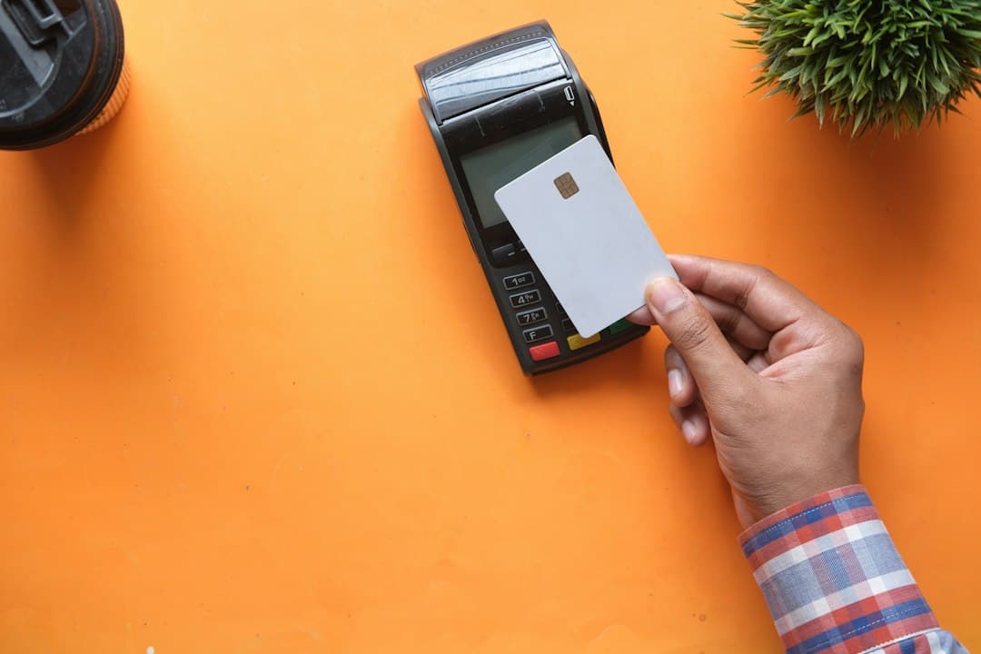 Main insérant une carte bancaire blanche dans un terminal de paiement sur fond orange.