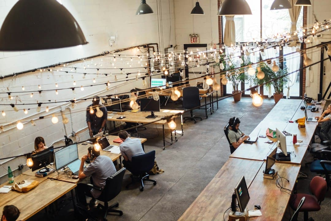 Freelanceurs travaillant sur des ordinateurs portables dans un espace de coworking lumineux avec guirlandes et plantes.