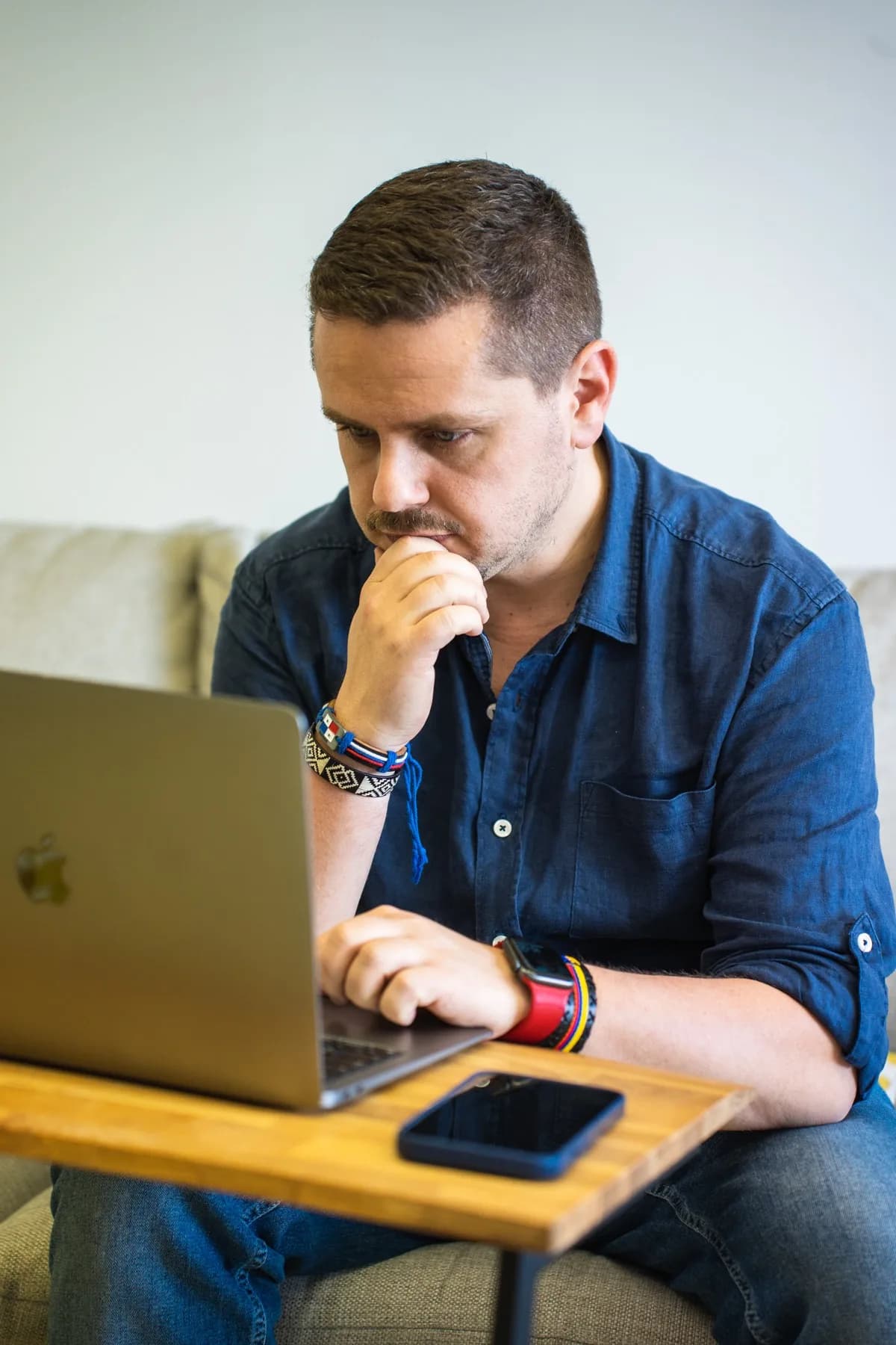 Cédric Tumminello focused on his MacBook, hand on his chin, sitting on a couch