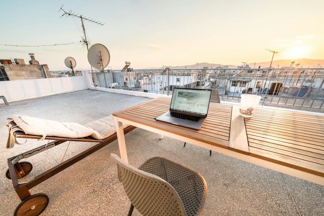Laptop on a terrace table overlooking the rooftops of a Spanish city at sunset.