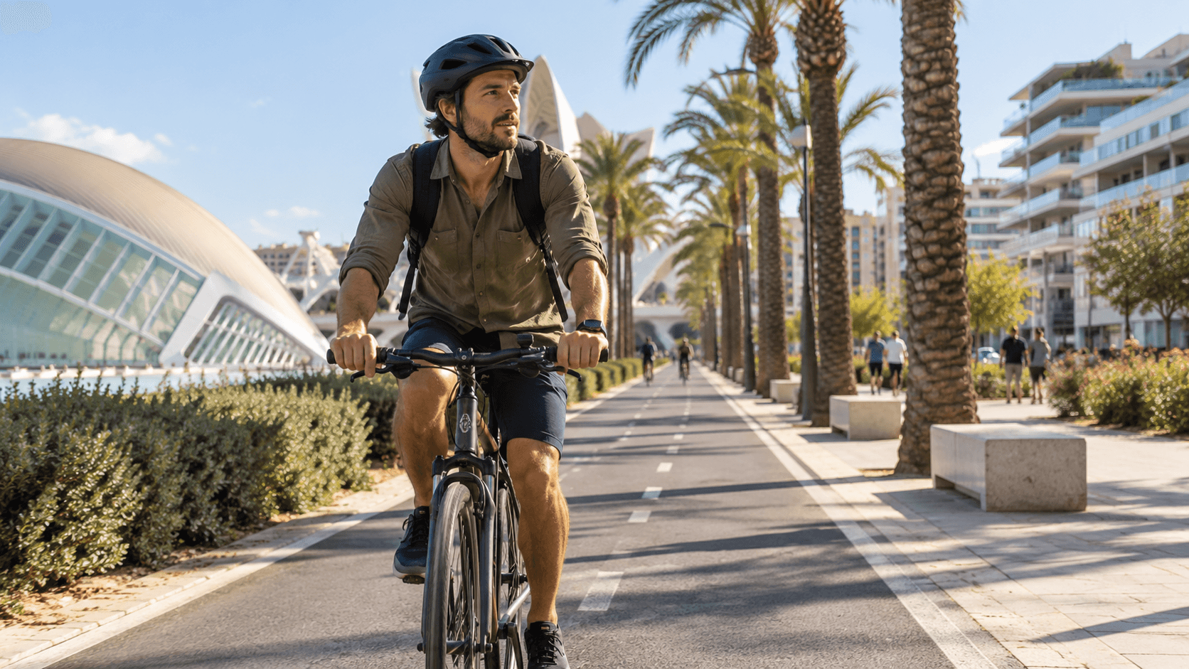 Cyclist riding on a dedicated bike lane in a Spanish city with palm trees and modern buildings.