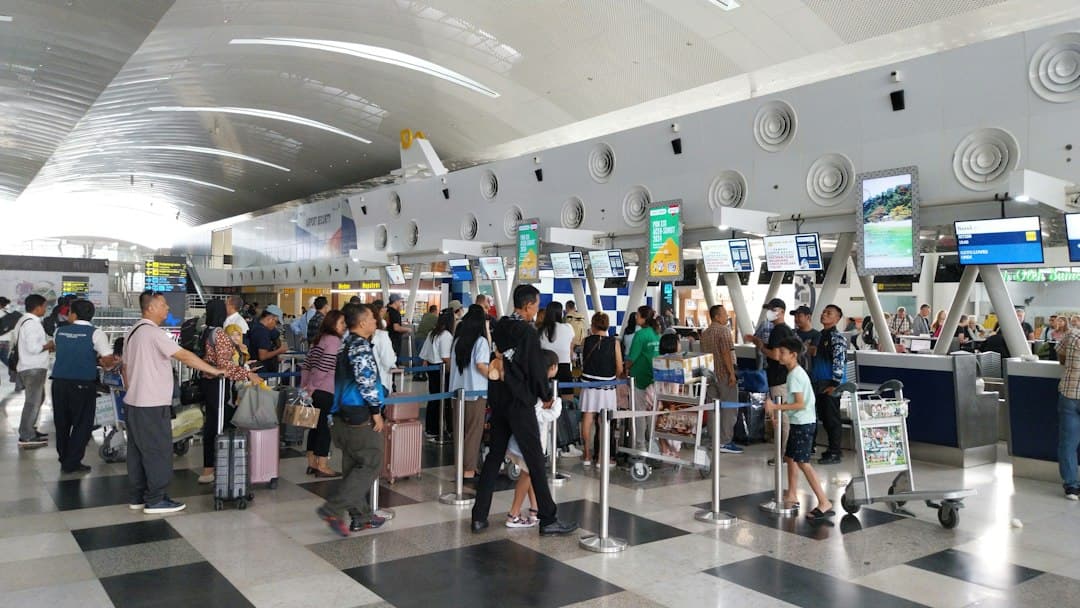 Crowded airport check-in hall with travelers, luggage and service counters during peak hours.