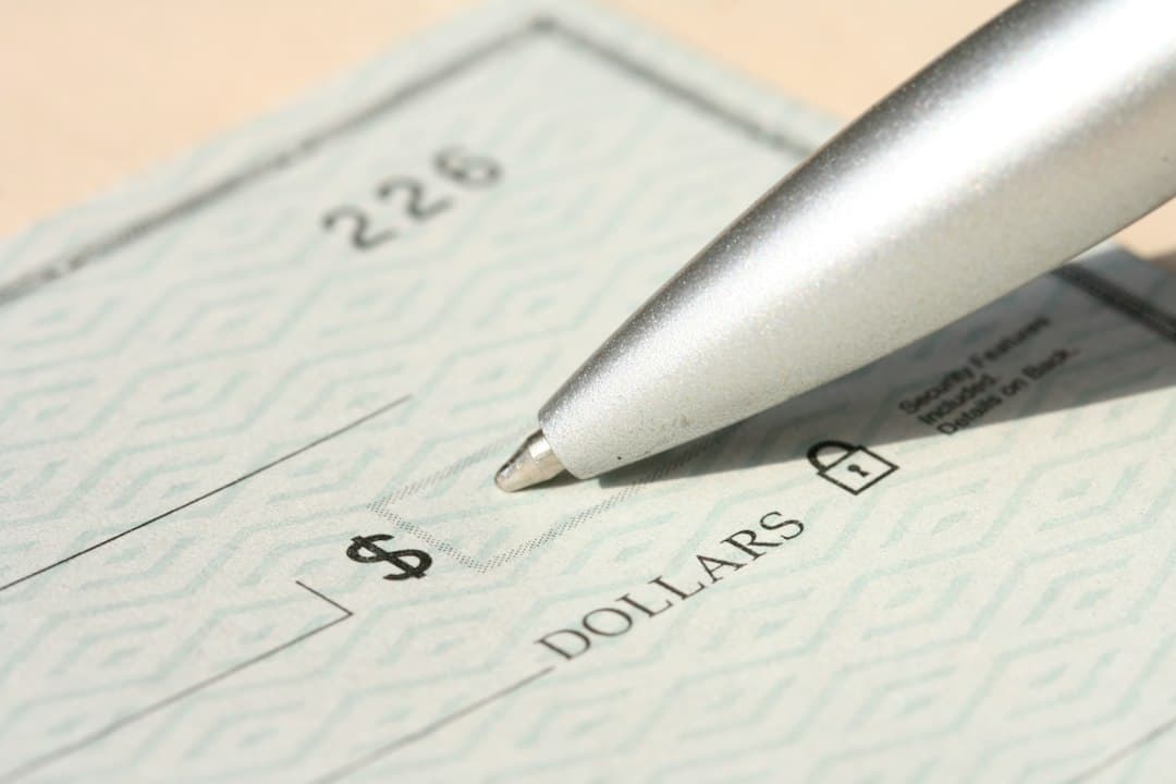 Silver pen hovering over a bank check with a dollar amount visible on a desk.