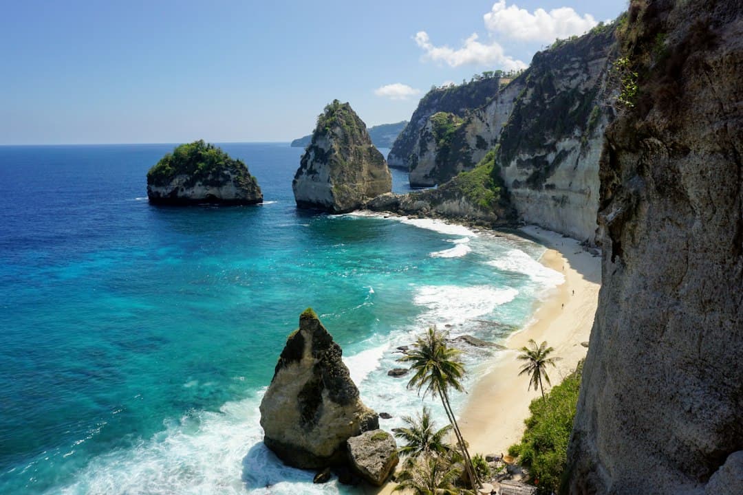 Strand op Bali met wit zand, brekende golven en imposante kalksteenkliffen onder een blauwe lucht.
