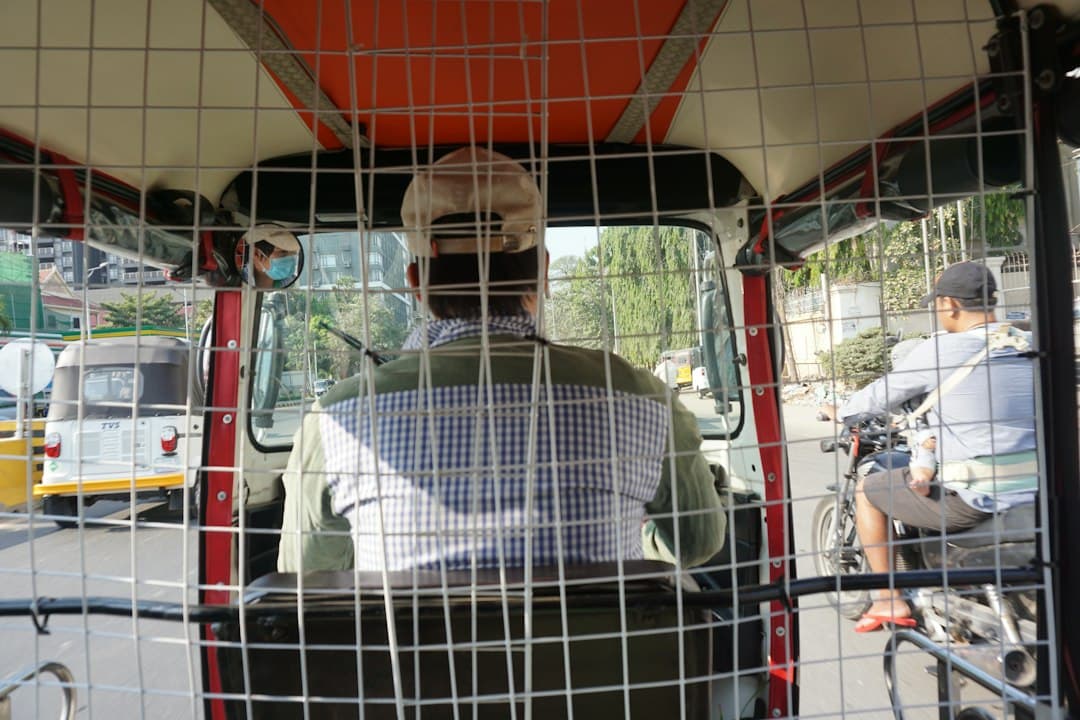 Interior of a tuk-tuk with metal protective grilles, driver visible through the mesh, street scene in Phnom Penh.