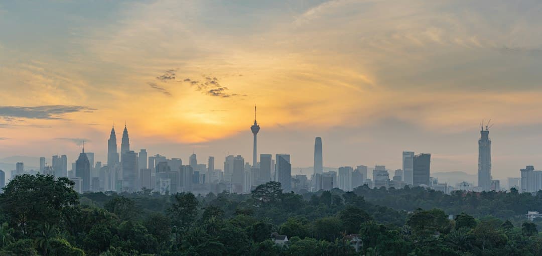 Skyline de Kuala Lumpur à l'heure dorée avec les tours Petronas et gratte-ciel au-dessus de la végétation verte.