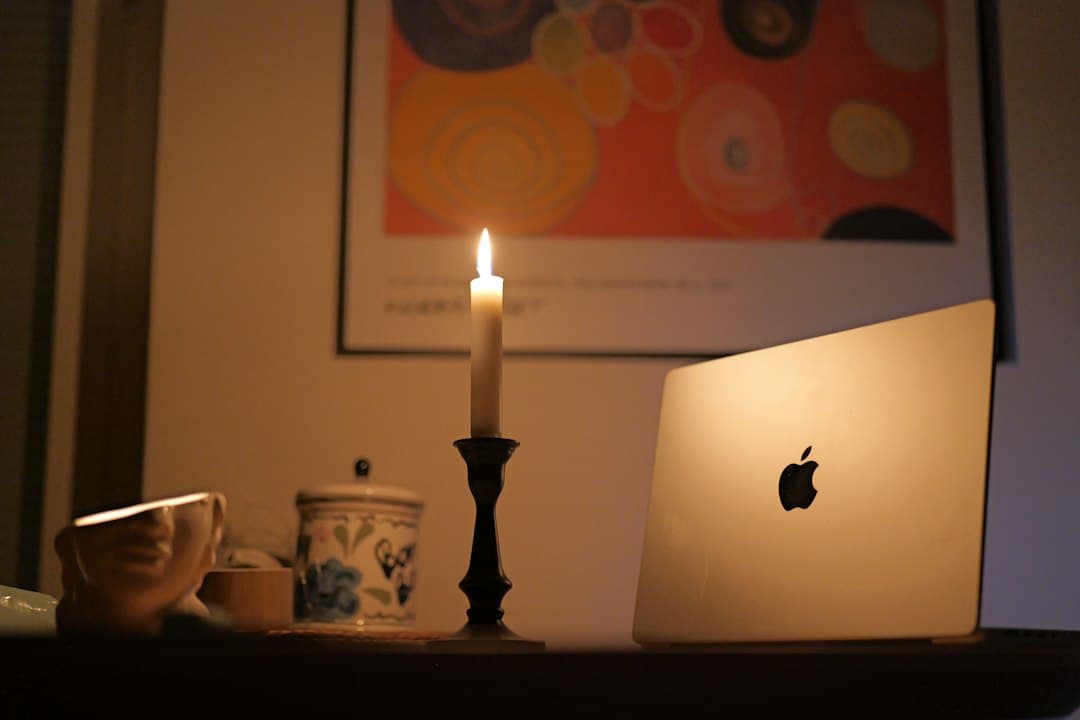 Laptop lit by candlelight on a desk during a power outage, with a cup nearby.