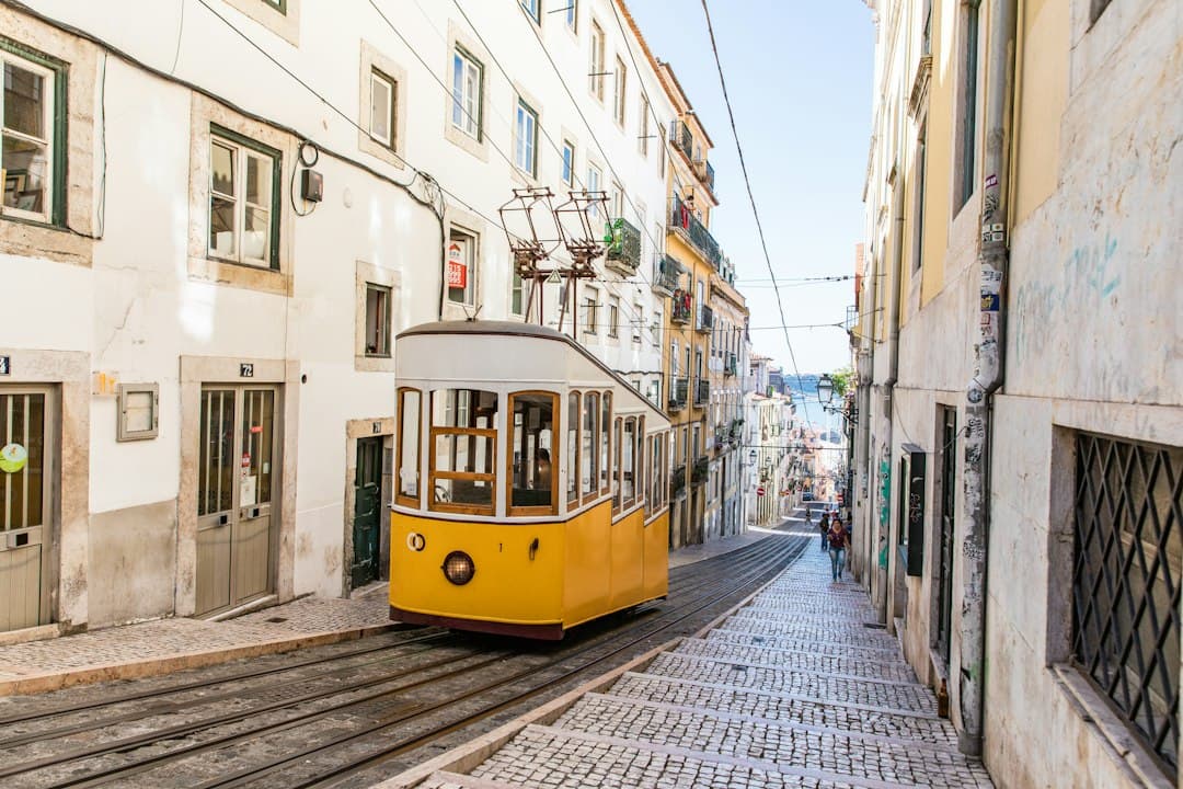 Yellow tram on a cobbled street in Lisbon with historic buildings, representing public transportation in Portugal.
