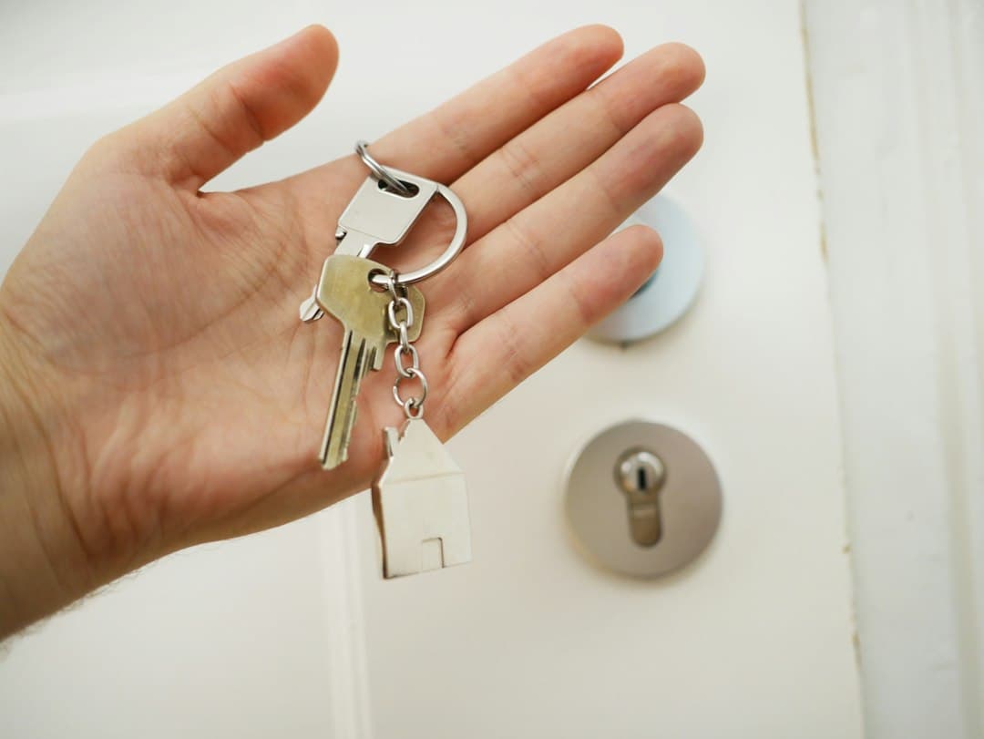A hand holding house keys with a house-shaped keychain in front of a door.