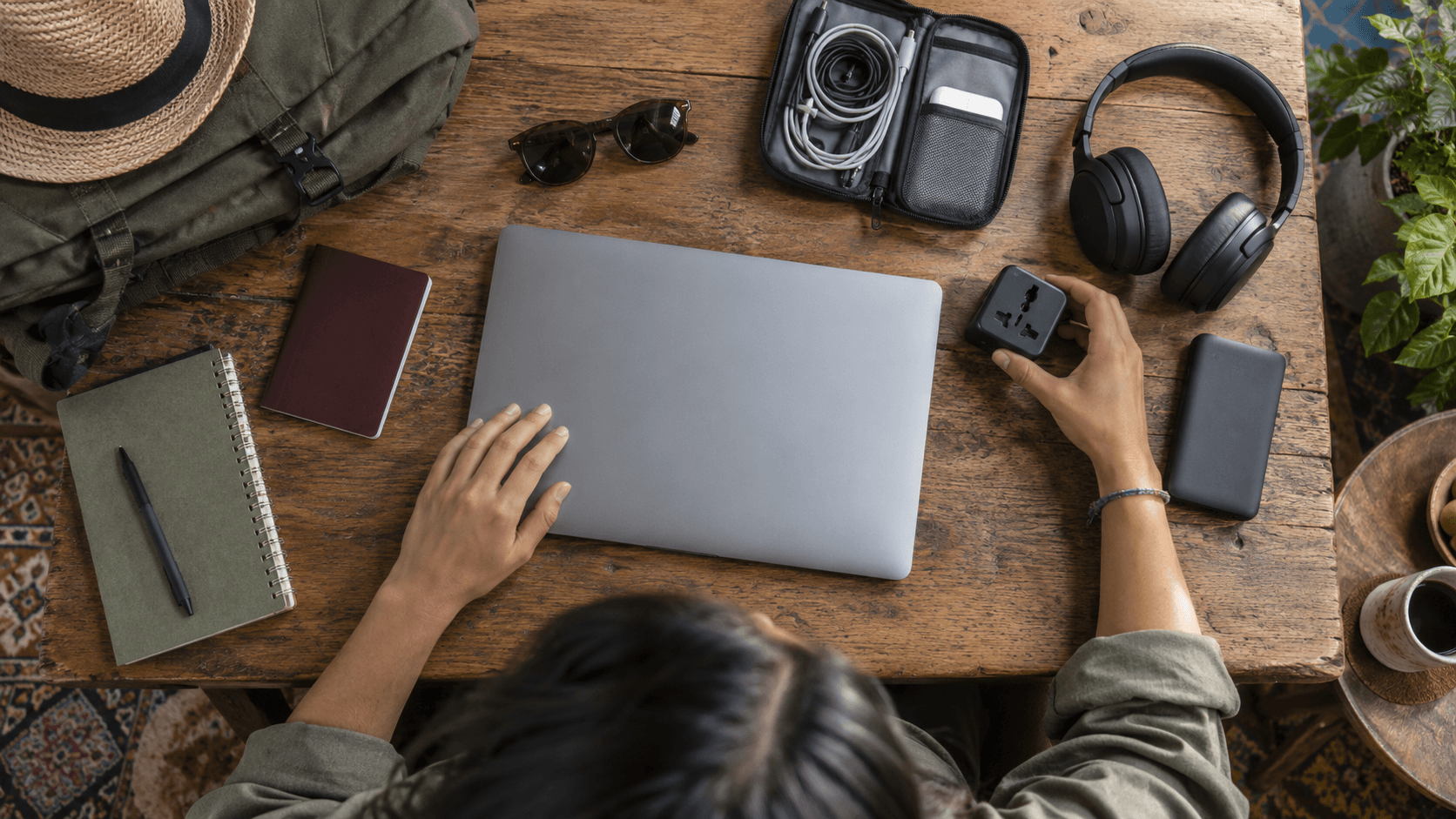 Digital nomad workspace with laptop, headphones, camera and travel documents on a wooden table.