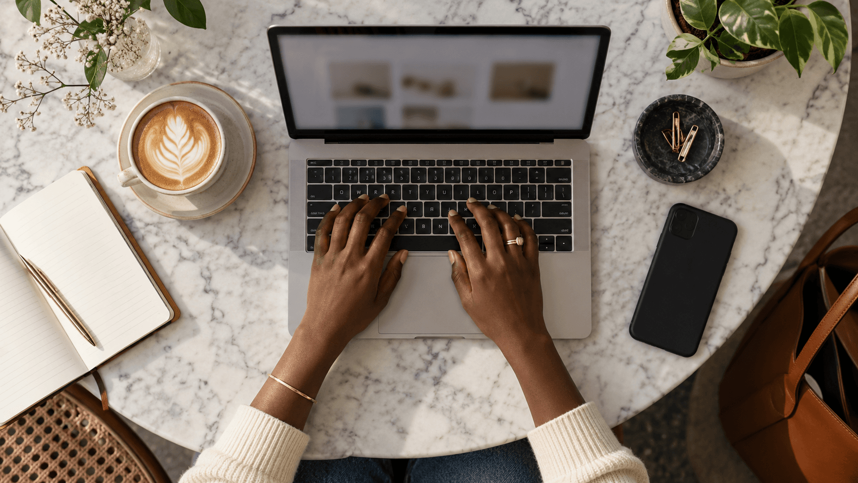 Remote worker typing on a laptop at a café table with a cup of coffee and a notebook