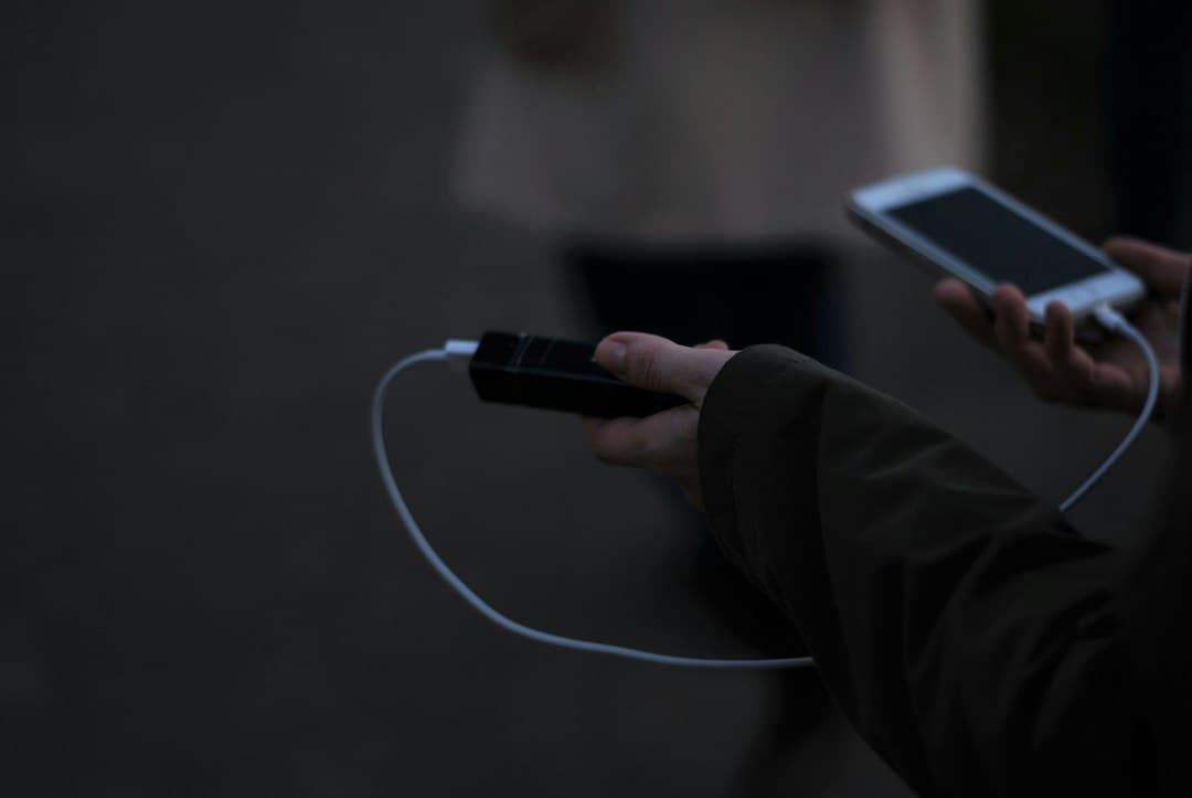 Personne tenant une batterie externe connectée à un smartphone via câble USB pour la recharge.