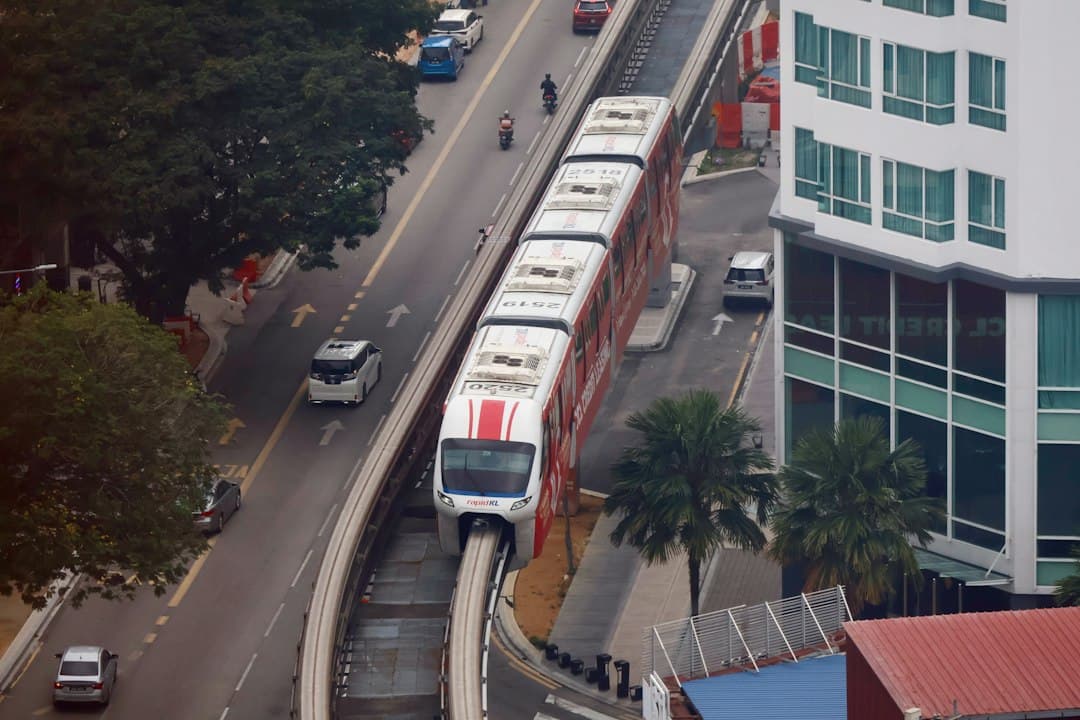 Elevated monorail train on an overhead track above a Kuala Lumpur street with buildings and traffic.