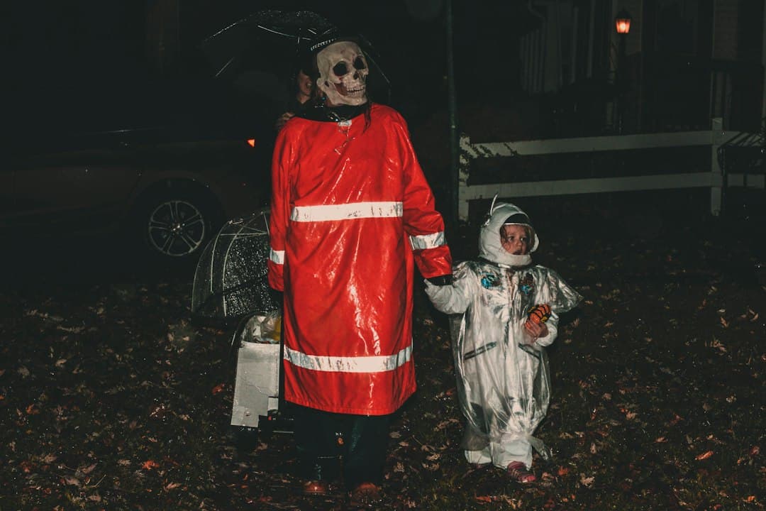 Enfants en costumes d'Halloween marchant la nuit, l'un portant un gilet rouge vif avec bandes réfléchissantes.